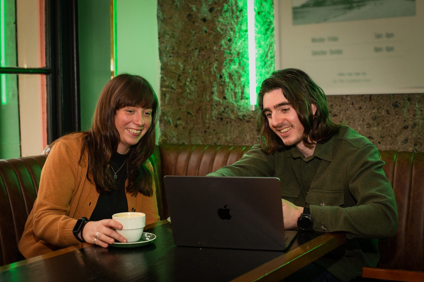 Ben Ó Mathúin working alongside a client at a café, reviewing work on a laptop